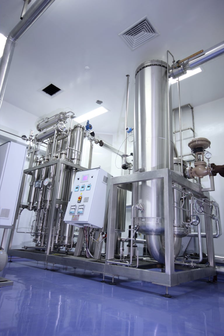 Industrial stainless steel fermentation or processing equipment with control panel in a clean manufacturing facility with blue flooring